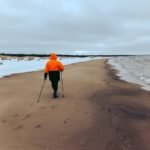 a person in orange jacket and black pants walking on beach