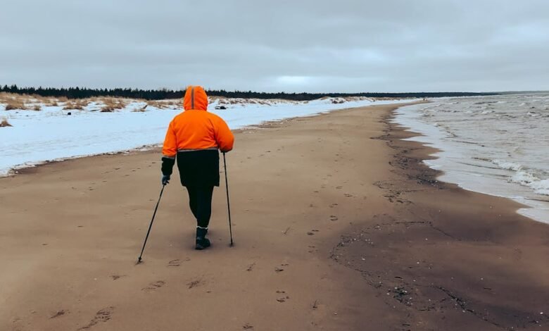 a person in orange jacket and black pants walking on beach