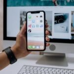 holding a smartphone in front of an imac