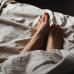 crop unrecognizable female feet lying in cozy bed