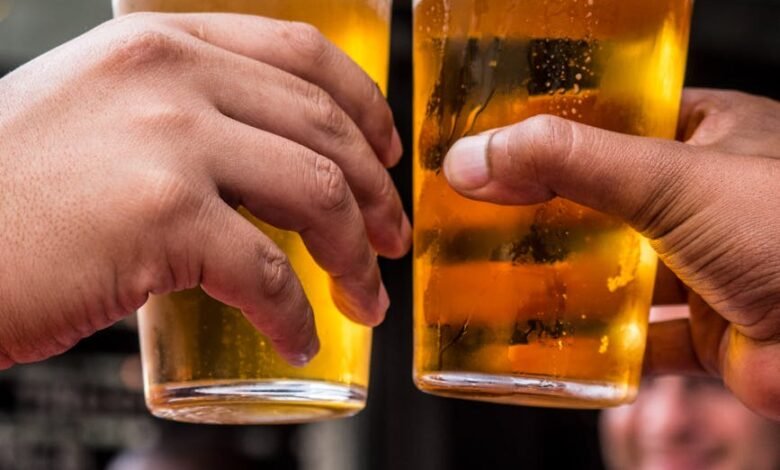 two persons holding drinking glasses filled with beer