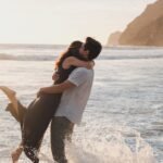 man picking up a woman while standing ankles deep in the sea