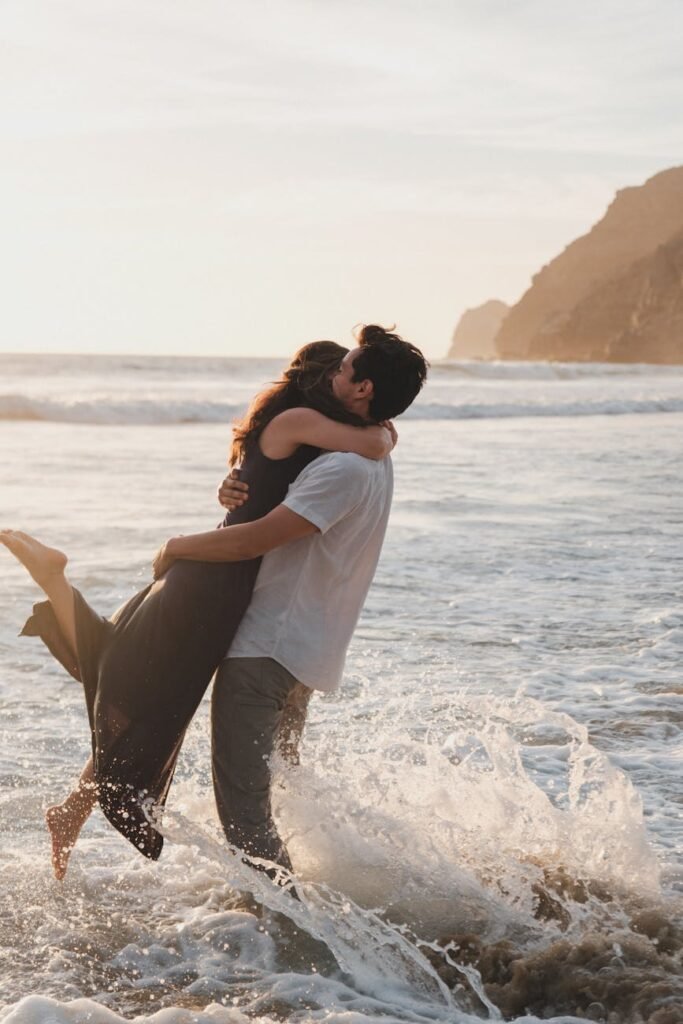 man picking up a woman while standing ankles deep in the sea