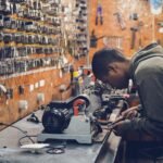 man in grey hoodie jacket holding black metal near white socket power supply